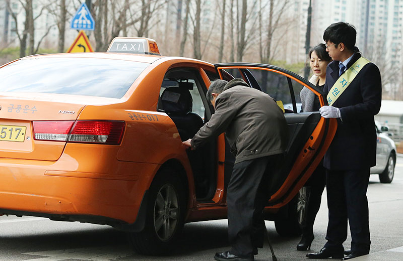 구매팀 박창재 사원(오른쪽)이 3월 11일 현관 손맞이 봉사활동에 참여해 거동이 불편한 고객의 택시 탑승을 돕고 있다.
